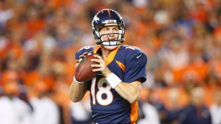 HD desktop wallpaper featuring a focused quarterback in a blue and orange uniform, poised to throw a football, with a vibrant crowd in the background.