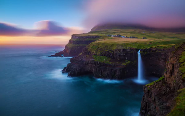 Gásadalur sunset over rugged cliffs and Atlantic, a waterfall plunging from a grassy plateau into the sea — HD PC desktop wallpaper/background showcasing earth and a small man-made village.