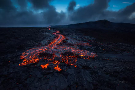 A breathtaking HD wallpaper showcasing molten lava flowing down a Hawaiian volcano, set against a dramatic, cloudy sky, highlighting the raw power and beauty of nature.