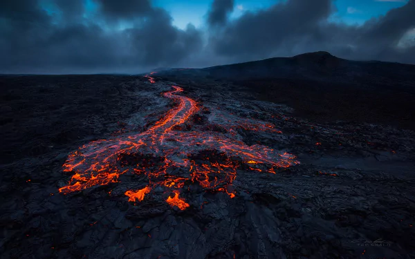A breathtaking HD wallpaper showcasing molten lava flowing down a Hawaiian volcano, set against a dramatic, cloudy sky, highlighting the raw power and beauty of nature.
