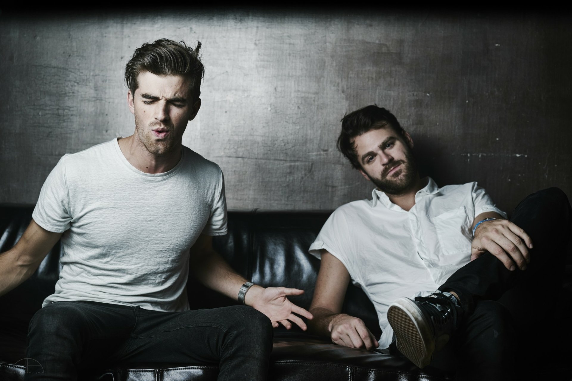 HD desktop wallpaper of The Chainsmokers, featuring two members casually seated against a moody backdrop.