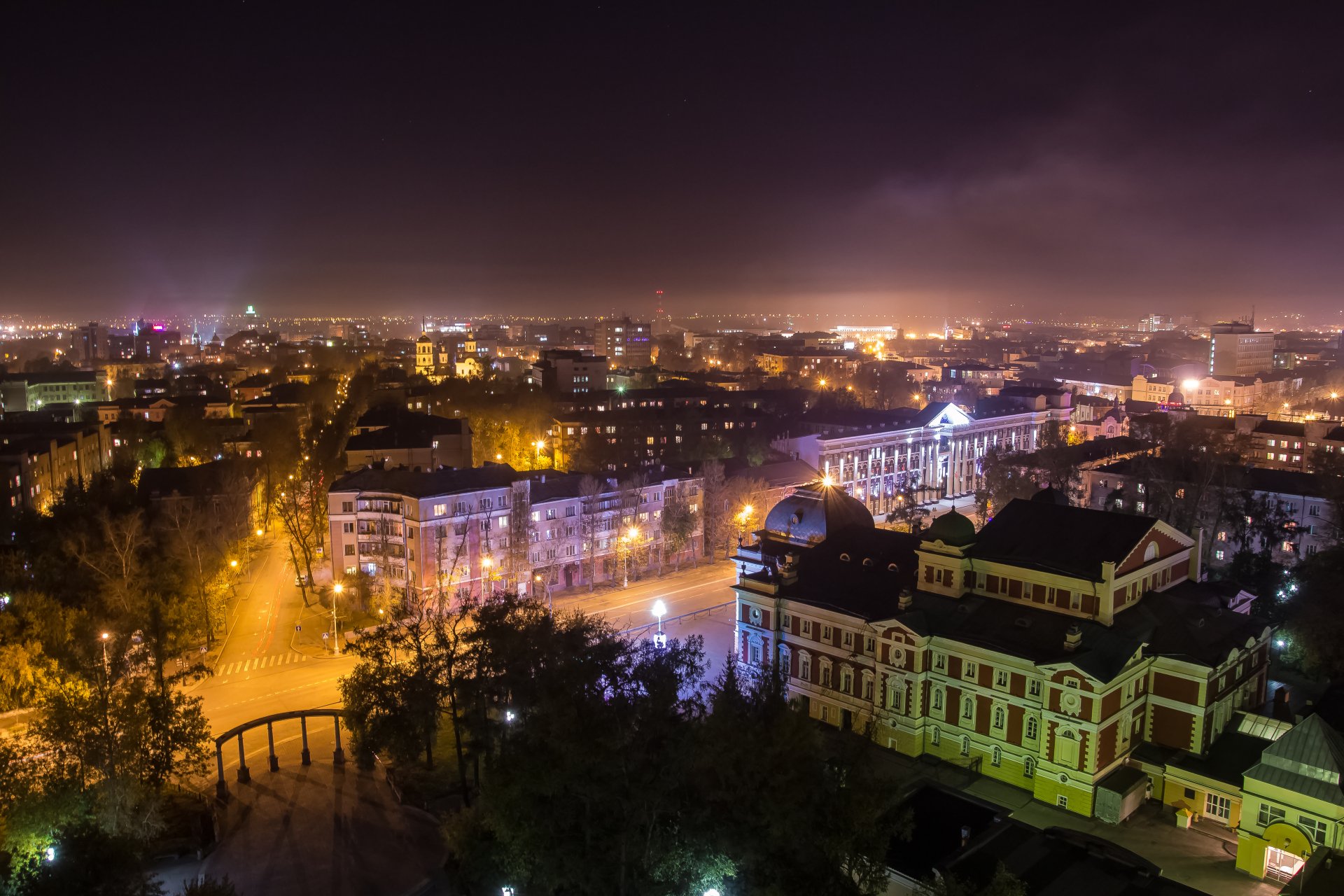 Panoramic night view of illuminated street and historic architecture in Irkutsk, Russia, captured in 4K Ultra HD with city lights glowing under a cloudy sky.