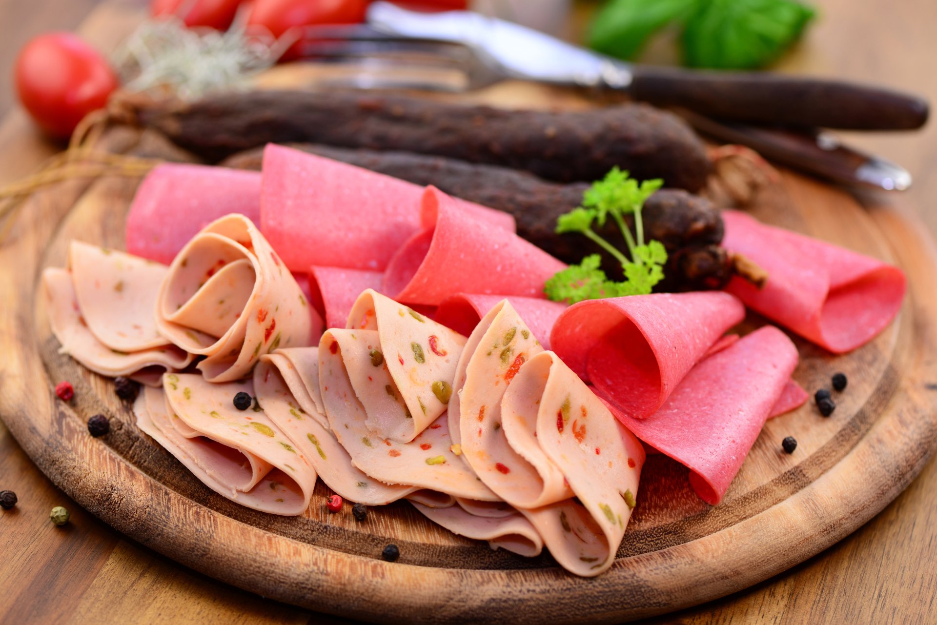 4K Ultra HD desktop wallpaper featuring an assortment of sliced deli meats and sausages arranged on a wooden board with fresh herbs and cherry tomatoes.
