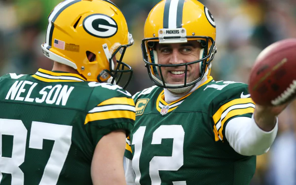 Green Bay Packers player wearing jersey number 12 smiles while holding a football, with another player in the foreground, as a HD desktop wallpaper.