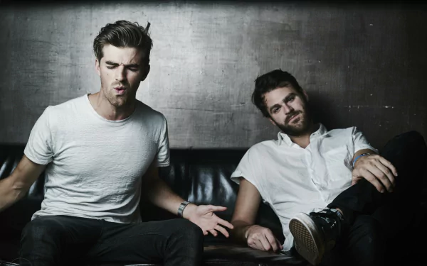HD desktop wallpaper of The Chainsmokers, featuring two members casually seated against a moody backdrop.