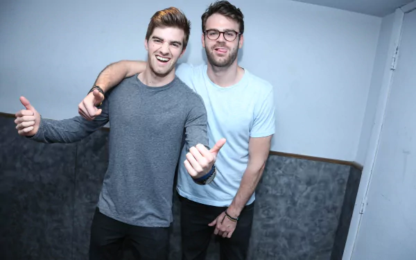 HD desktop wallpaper of The Chainsmokers, featuring two members posing with thumbs up in a casual setting.