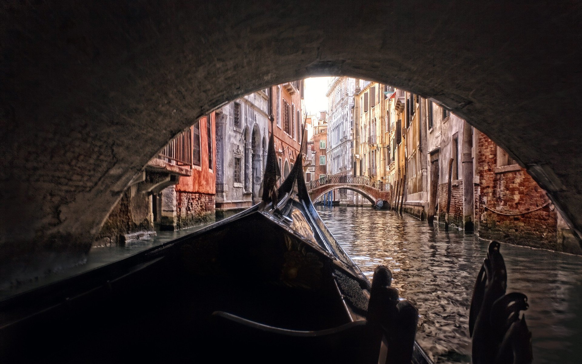 View from a gondola navigating a narrow canal in Venice, Italy, surrounded by historic houses and arched bridges, captured in HD for a desktop wallpaper.