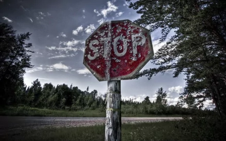 A weathered stop sign stands prominently beside a grassy road, set against a dramatic sky, creating a striking artistic desktop wallpaper background.
