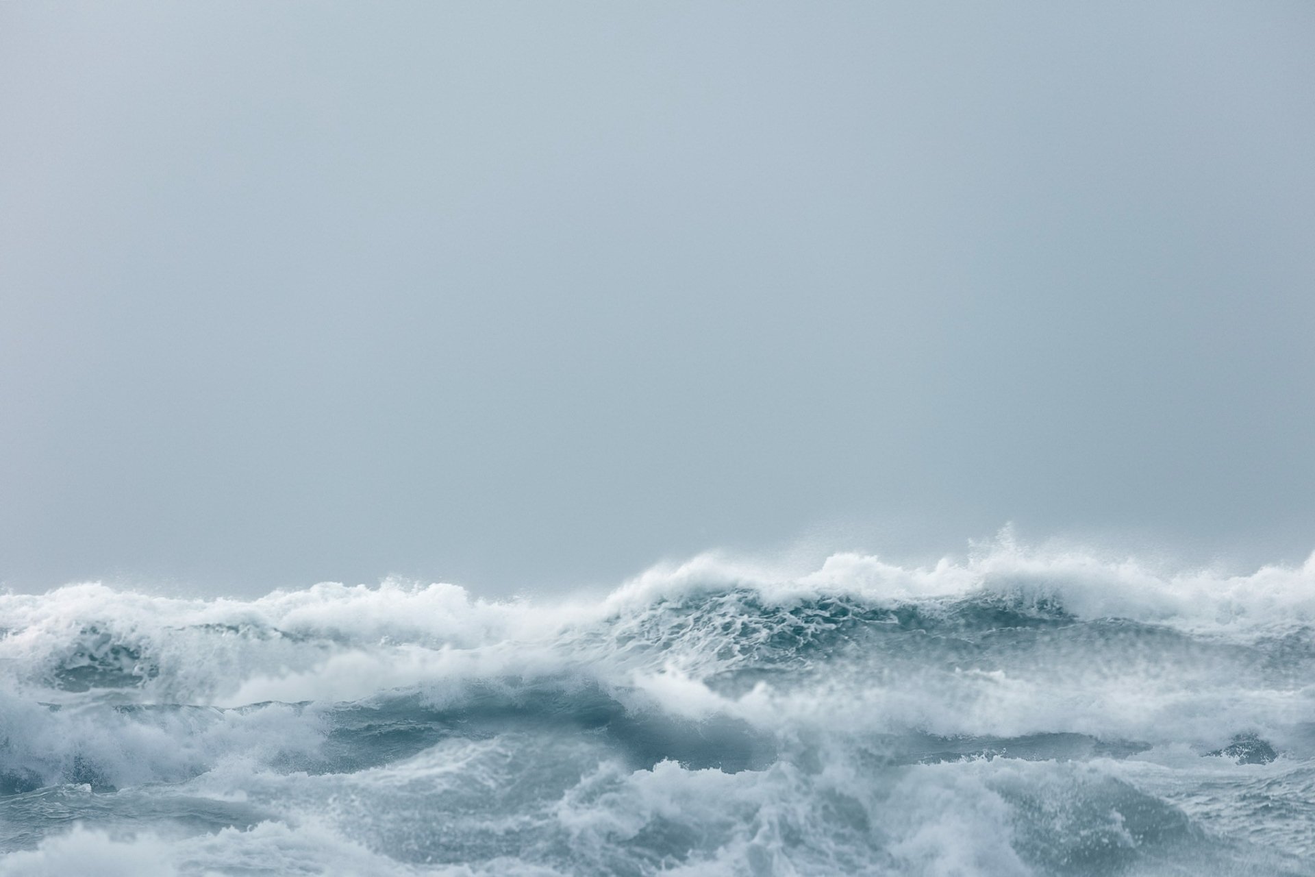 HD desktop wallpaper of a natural ocean scene featuring waves with white foam under a pale, overcast sky.