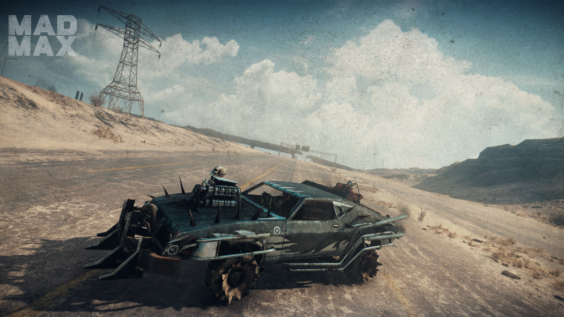 A high-definition desktop wallpaper and background featuring a dystopian landscape from Mad Max: Fury Road video game, showcasing a rugged, armored car on a deserted road under a vast, cloudy sky.