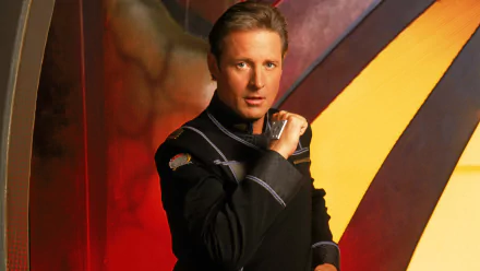 Man in a dark command uniform poses against a red-and-gold abstract backdrop — HD Babylon 5: Thirdspace desktop wallpaper.