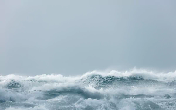 HD desktop wallpaper of a natural ocean scene featuring waves with white foam under a pale, overcast sky.