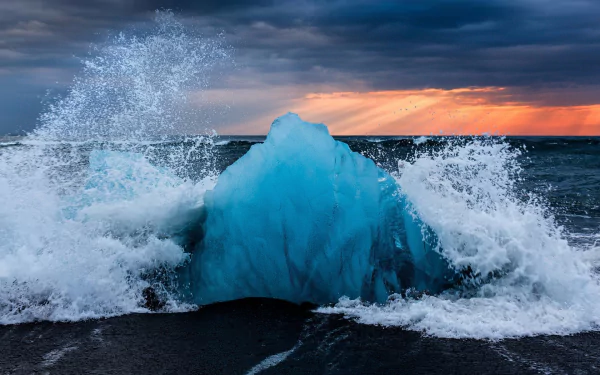 HD desktop wallpaper showing a frozen blue iceberg in the ocean with waves crashing under a dramatic winter sky on the horizon.
