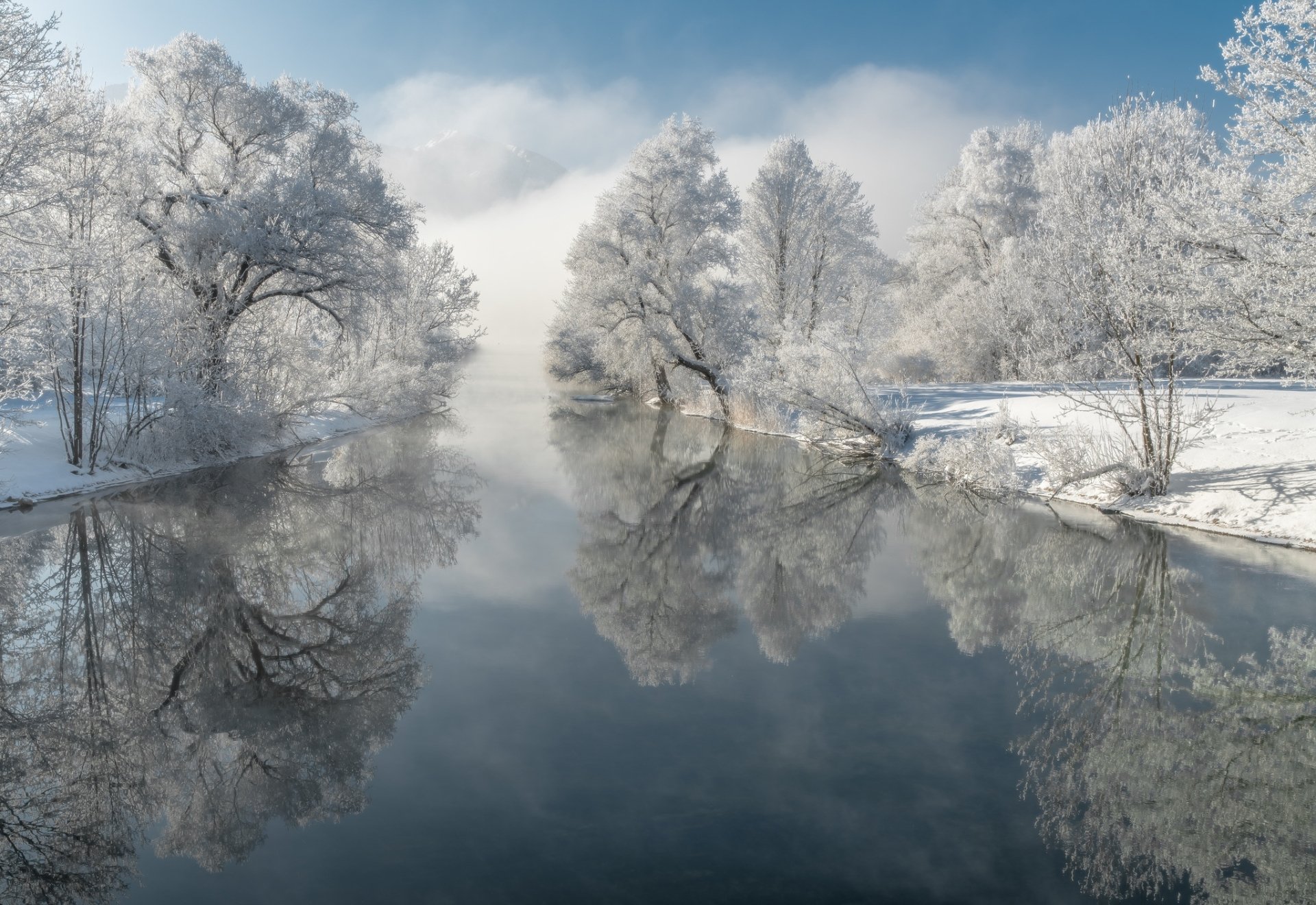 A serene winter river scene with snow-covered trees and thick fog, reflecting perfectly on the calm water, captured in HD for a nature desktop wallpaper.