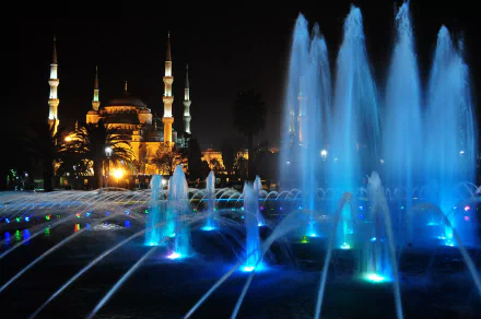 Illuminated Sultan Ahmed Mosque and vibrant blue-lit fountain at night in Istanbul, Turkey, showcasing a serene religious and architectural scene.