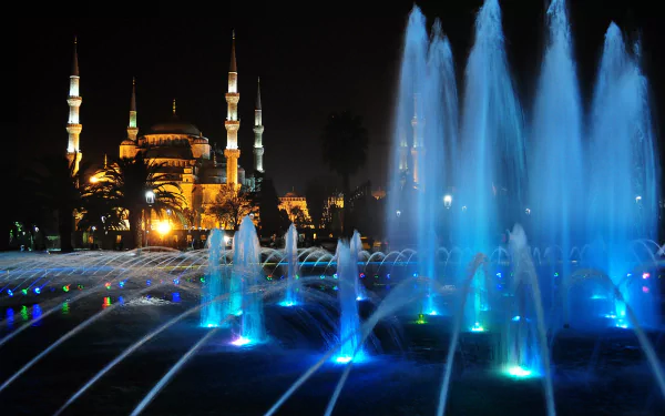 Illuminated Sultan Ahmed Mosque and vibrant blue-lit fountain at night in Istanbul, Turkey, showcasing a serene religious and architectural scene.