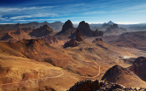Winding road through the rugged Hoggar Mountains in the Tassili N'Ajjer region of Assekrem, Algeria, showcasing dramatic desert mountain landscapes under a blue sky.