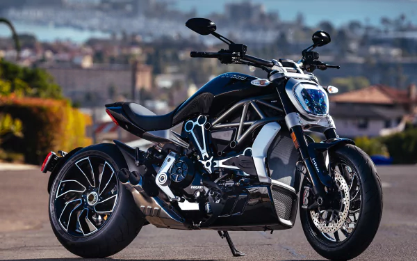 A sleek Ducati Diavel motorcycle parked outdoors, showcased as an HD PC desktop wallpaper and background with a blurred cityscape in the background.