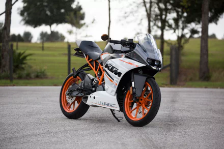 A sharp and striking KTM motorcycle is parked on a paved surface with lush green scenery in the background, captured in HD quality for a dynamic desktop wallpaper and background.