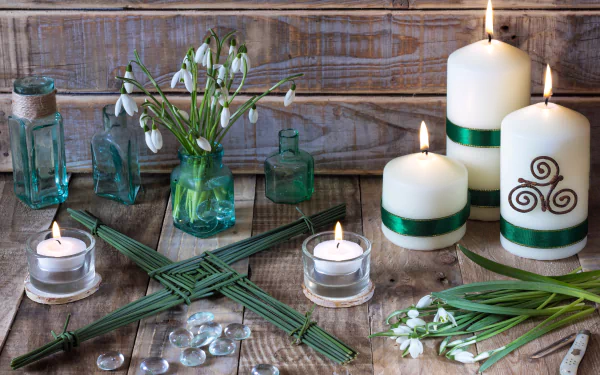 Zen still-life photography of lit candles, snowdrops in glass vases, green ribbon and glass pebbles on weathered wood — 5K Ultra HD PC desktop wallpaper/background.