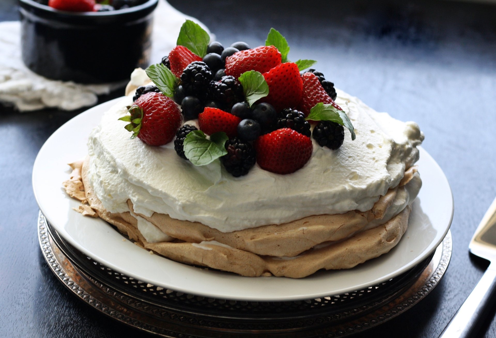 Pavlova with whipped cream topped by strawberries, raspberries and blueberries on a plate — vibrant berry pastry captured as a 2K Quad HD PC desktop wallpaper/background.