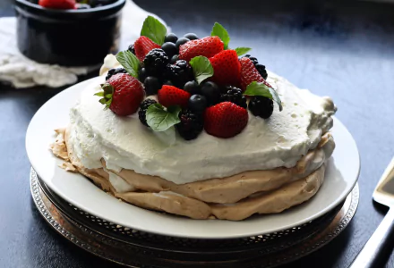 Pavlova with whipped cream topped by strawberries, raspberries and blueberries on a plate — vibrant berry pastry captured as a 2K Quad HD PC desktop wallpaper/background.