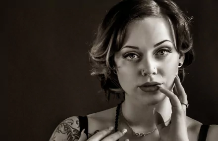 Sepia black-and-white HD PC desktop wallpaper: close-up portrait of a female model, short hair, hand to chin, face framed by soft lighting and a visible shoulder tattoo.