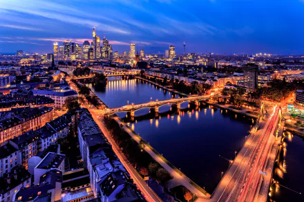 Nighttime cityscape of Frankfurt, Germany showcasing illuminated skyscrapers, buildings, and bridges over the river, captured as an HD PC desktop wallpaper background.