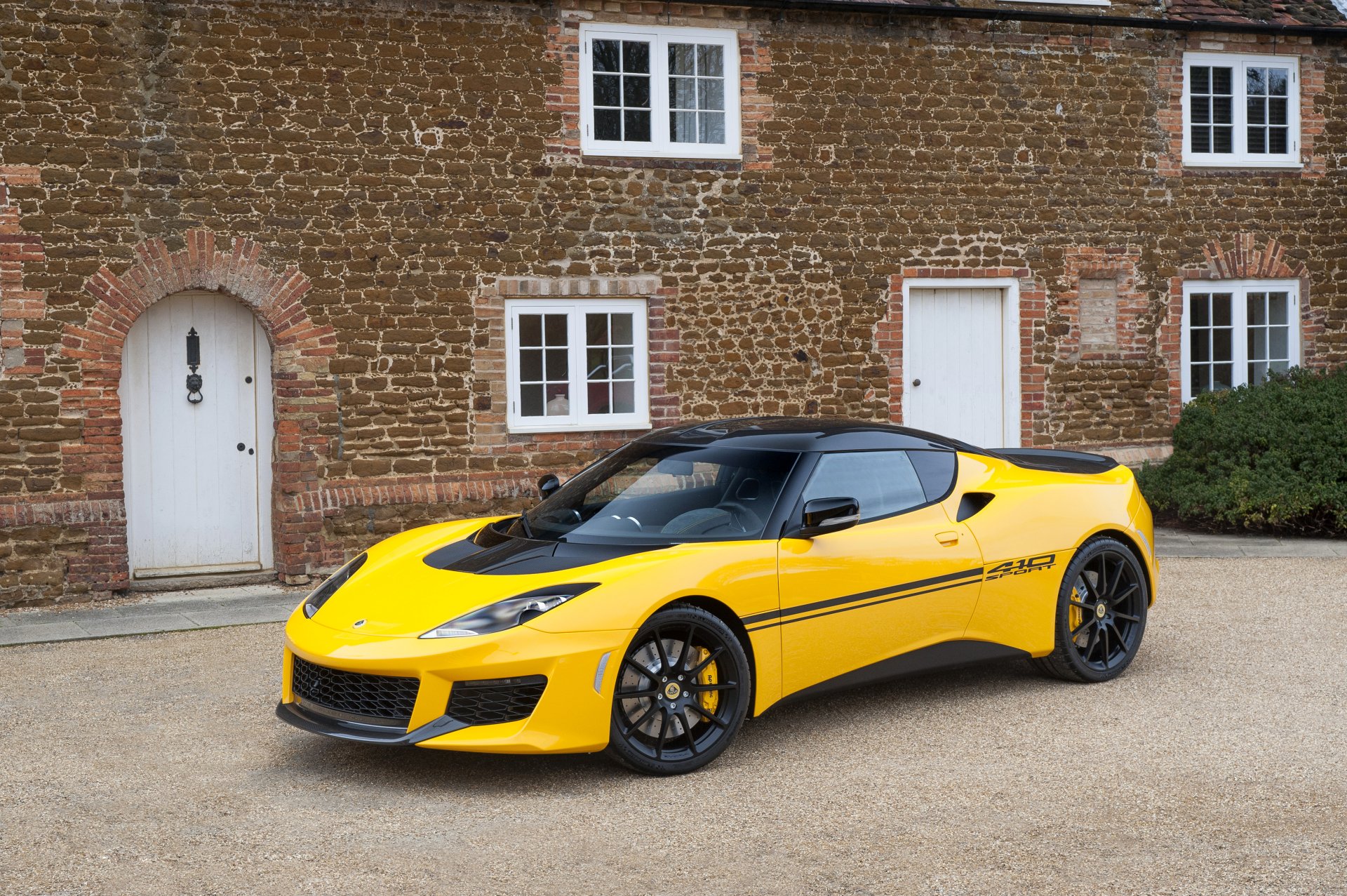 Yellow Lotus Evora supercar parked in front of a brick building, captured in 4K Ultra HD as a striking desktop wallpaper and background.