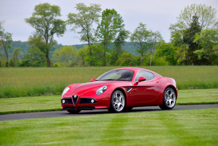 A red Alfa Romeo 8C Competizione parked on a grassy area with trees in the background, captured in 4K Ultra HD for PC desktop wallpaper.