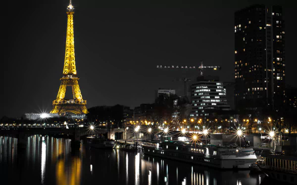 Nighttime view of the Eiffel Tower illuminated, reflecting on the Seine River in Paris with boats docked nearby and city lights enhancing the dark skyline.
