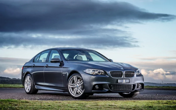 A silver BMW 5 Series car parked on a countryside road under a cloudy sky, showcased as an HD PC desktop wallpaper and background.