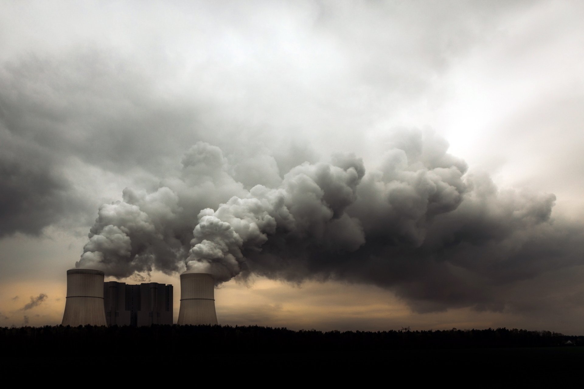 A striking image of a nuclear power plant, featuring towering cooling towers emitting dense smoke against a moody sky, serving as a thought-provoking desktop wallpaper.