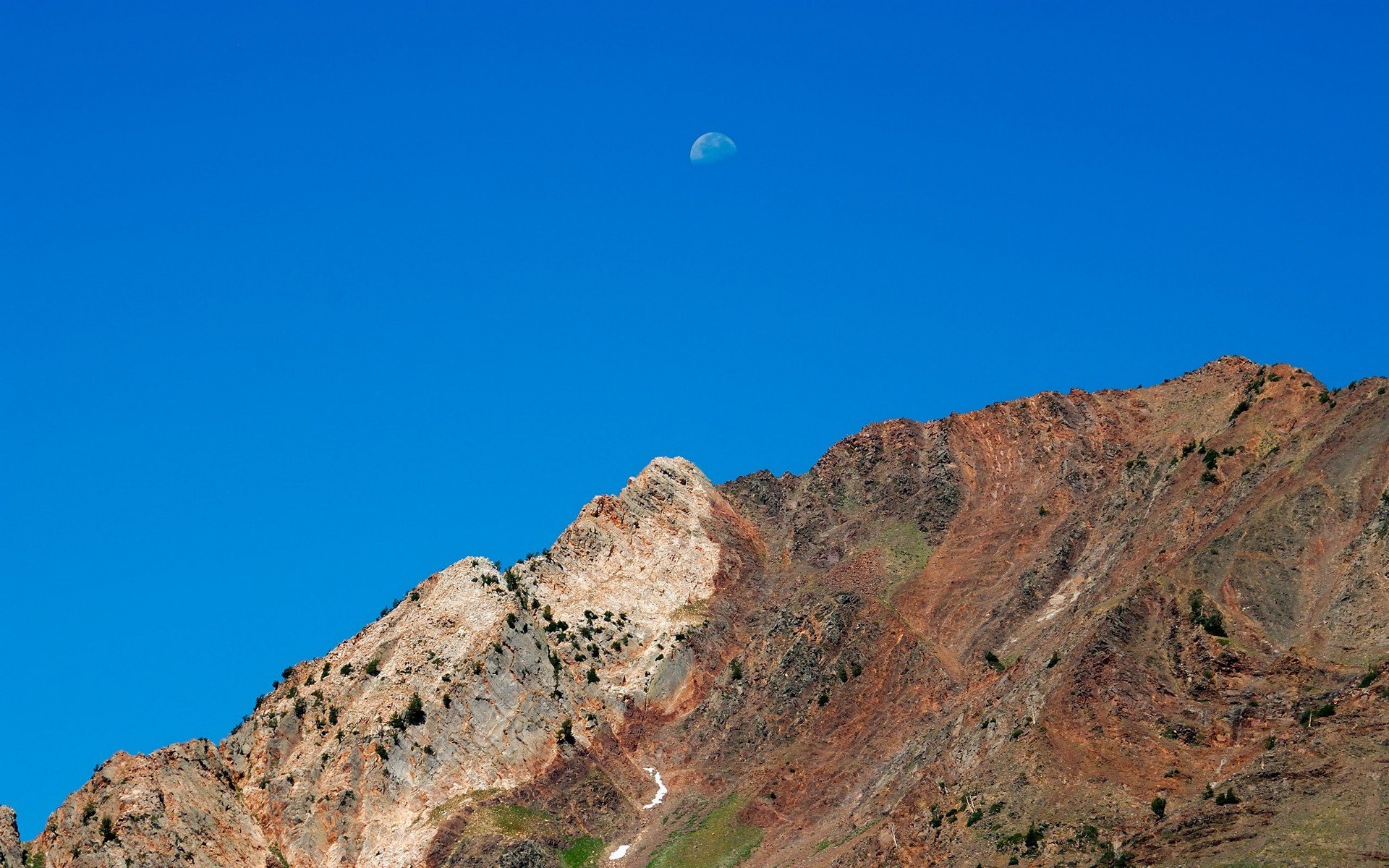 HD desktop wallpaper featuring a blue sky with a visible moon above rugged sandstone mountains in a natural landscape.