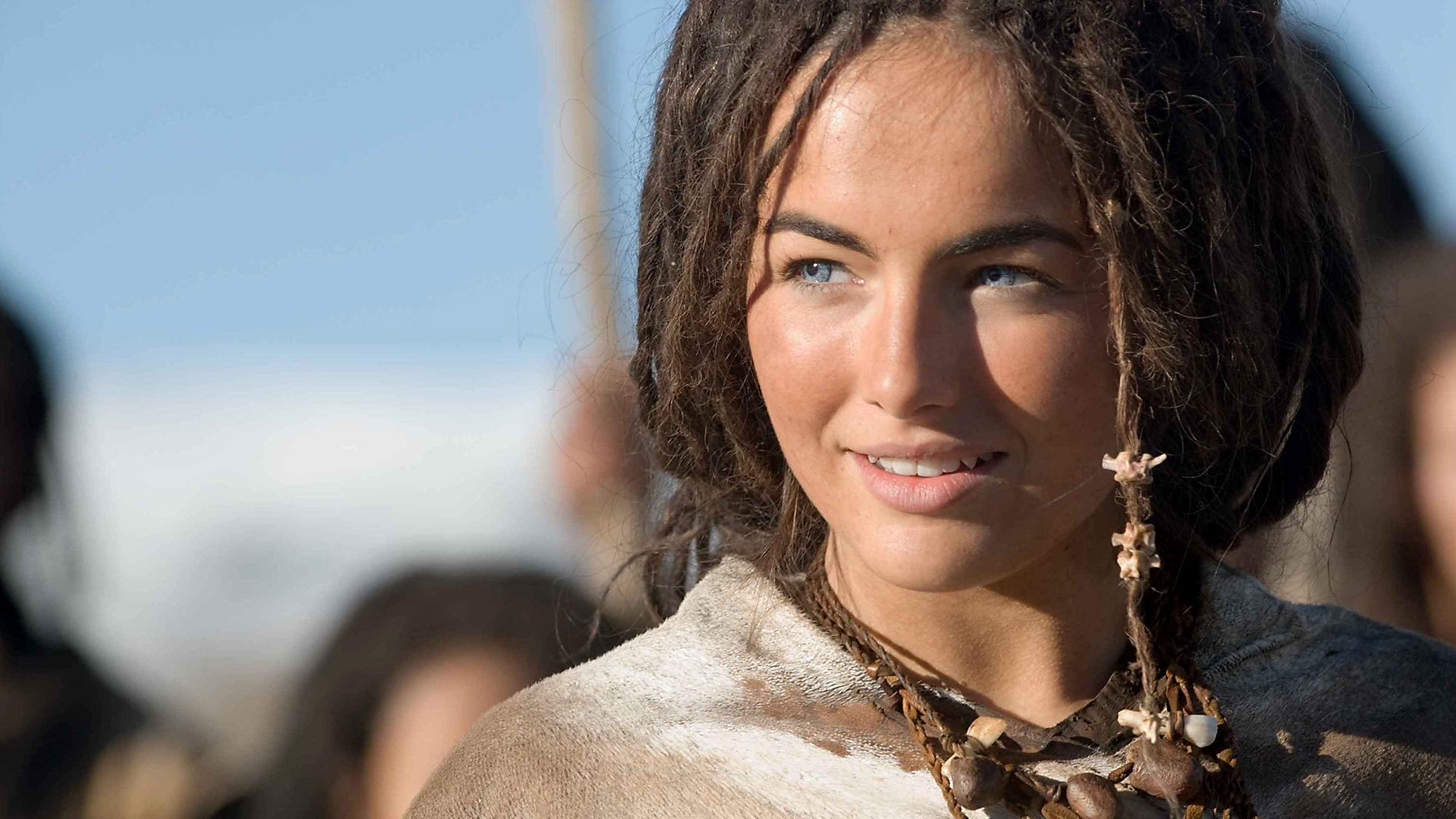 HD PC desktop wallpaper featuring a close-up of a smiling woman with dreadlocks from the movie 10,000 B.C., set against a soft blue sky background.