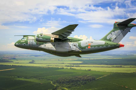 Embraer KC-390 military transport aircraft in flight over a green landscape under a partly cloudy sky, showcased as an HD PC desktop wallpaper.