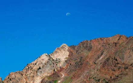 HD desktop wallpaper featuring a blue sky with a visible moon above rugged sandstone mountains in a natural landscape.