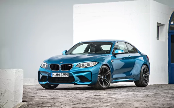 A blue BMW M2 sports car parked on a cobblestone driveway, showcased in a high-resolution 4K Ultra HD desktop wallpaper.