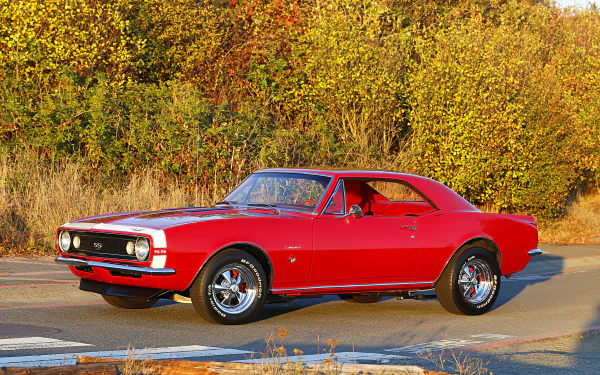 A vibrant red Chevrolet Camaro SS 350 muscle car and hot rod parked on a road with autumn foliage in the background, captured in an HD PC desktop wallpaper.