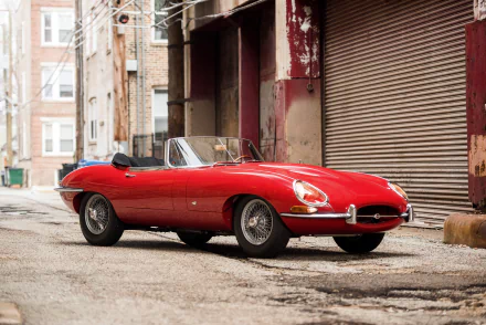 A vibrant red Jaguar E-Type supercar parked in an urban alley, captured in 4K Ultra HD as a striking PC desktop wallpaper and background.