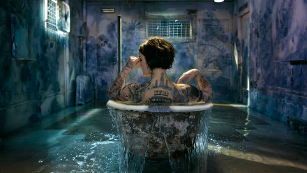 Brunette Jaimie Alexander with short hair, covered in tattoos, sits in a bath in a dim, water-filled room from the TV show Blindspot.