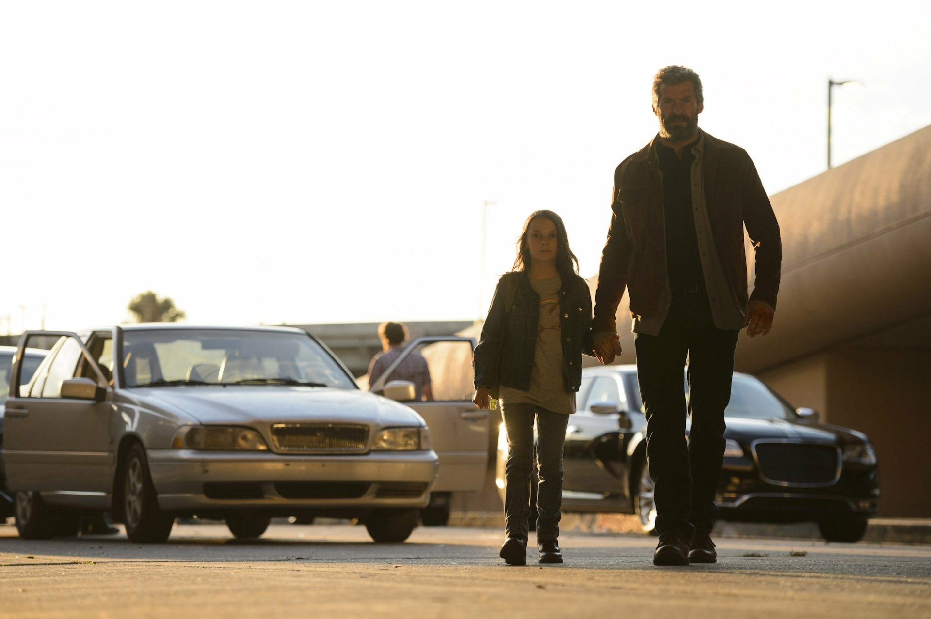 HD desktop wallpaper featuring a scene from the movie Logan with Dafne Keen as X-23 (Laura Kinney) and Hugh Jackman as Logan, walking on a street with cars in the background.