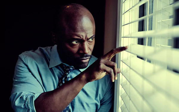 HD PC desktop wallpaper: intense scene from TV show Murder in the First — a man in shirt and tie peers through blinds, tense and alert.