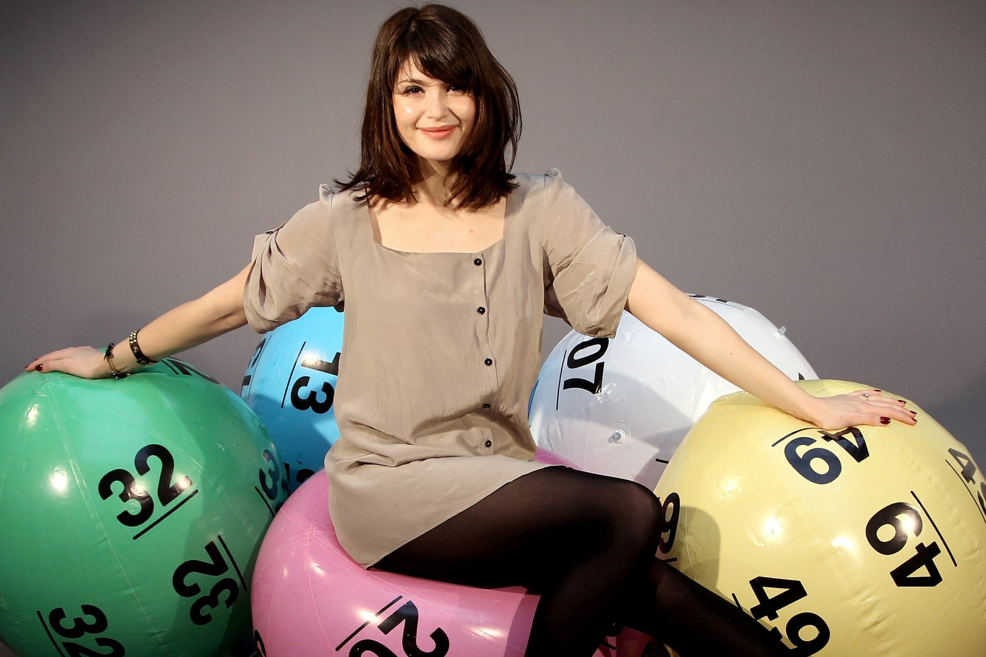 Actress and celebrity seated, smiling among oversized colorful lottery balls against a neutral backdrop — 2K Quad HD PC desktop wallpaper.