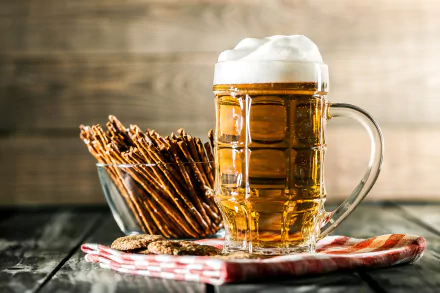 HD desktop wallpaper featuring a glass of frothy beer, pretzel sticks, and snacks on a wooden table with a checkered napkin, set against a rustic wooden background. Tags: alcohol, still life, food.