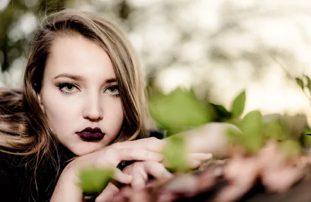 HD desktop wallpaper: close-up portrait of a woman model with green eyes and dark lipstick, face framed by soft bokeh and surrounding foliage.