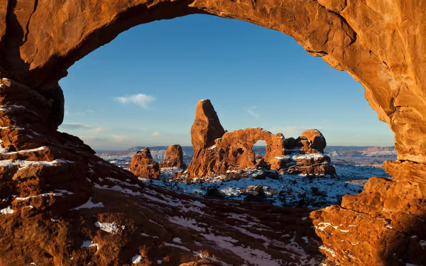 Snow-dusted sandstone formations framed by a natural arch in Arches National Park, Utah, under a clear winter sky in this HD wilderness landscape wallpaper.