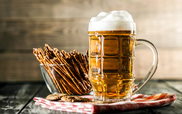 HD desktop wallpaper featuring a glass of frothy beer, pretzel sticks, and snacks on a wooden table with a checkered napkin, set against a rustic wooden background. Tags: alcohol, still life, food.