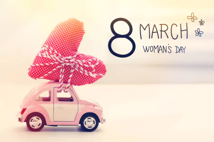 A pink toy car carrying a red heart tied with string, with 8 March Women's Day text, designed as a 4K Ultra HD PC desktop wallpaper celebrating the holiday.