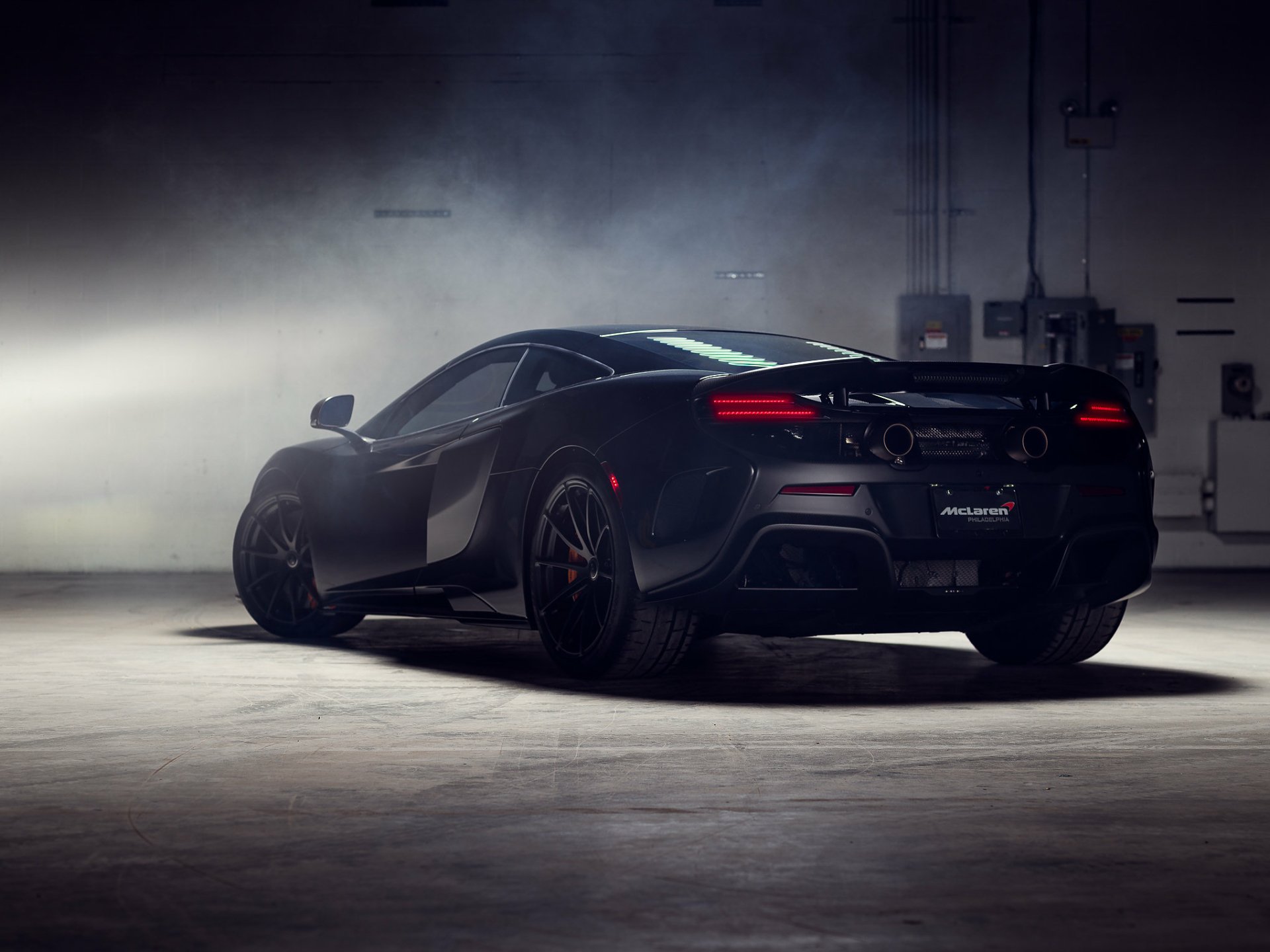 HD desktop wallpaper featuring a sleek black McLaren 675LT supercar in a dimly lit garage, highlighting its aggressive design and performance-focused build.